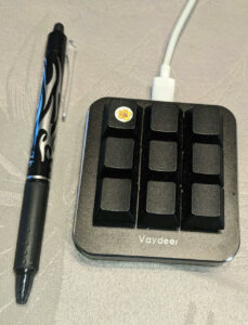 Foto: Quadratisches schwarzes Gehäuse 'Vaydeer' mit 9 Tasten ohne Aufdruck. Stift daneben ist doppelt so lang wie Gehäuse.